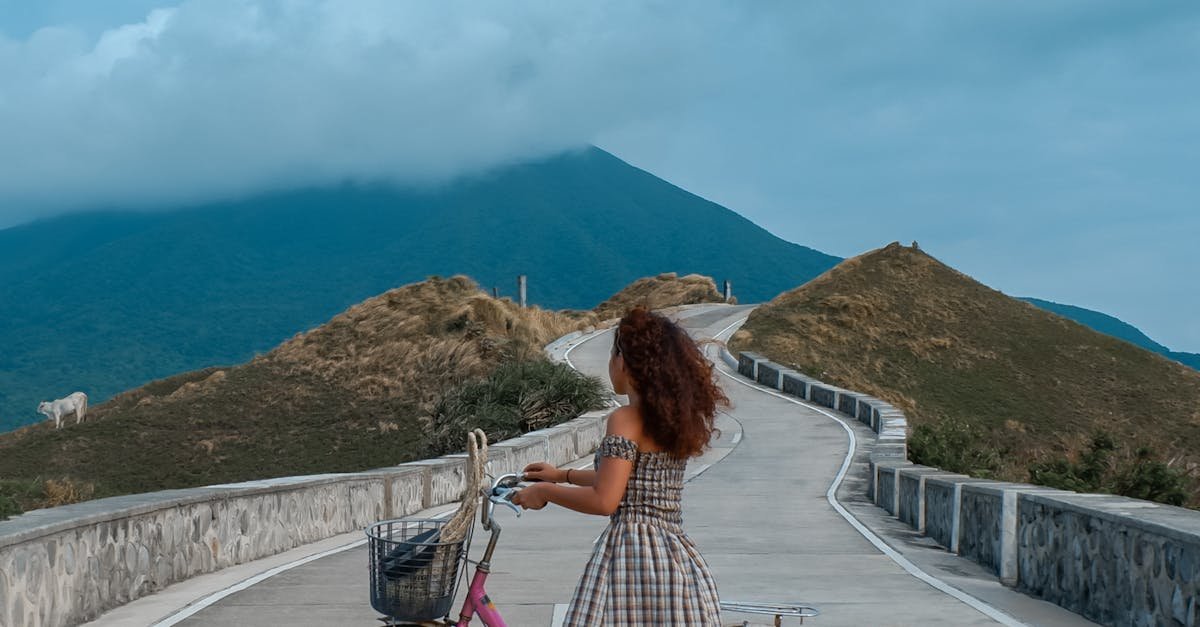 A woman stands with her bicycle on a winding road in Cagayan Valley, Philippines, with mountains in the background.