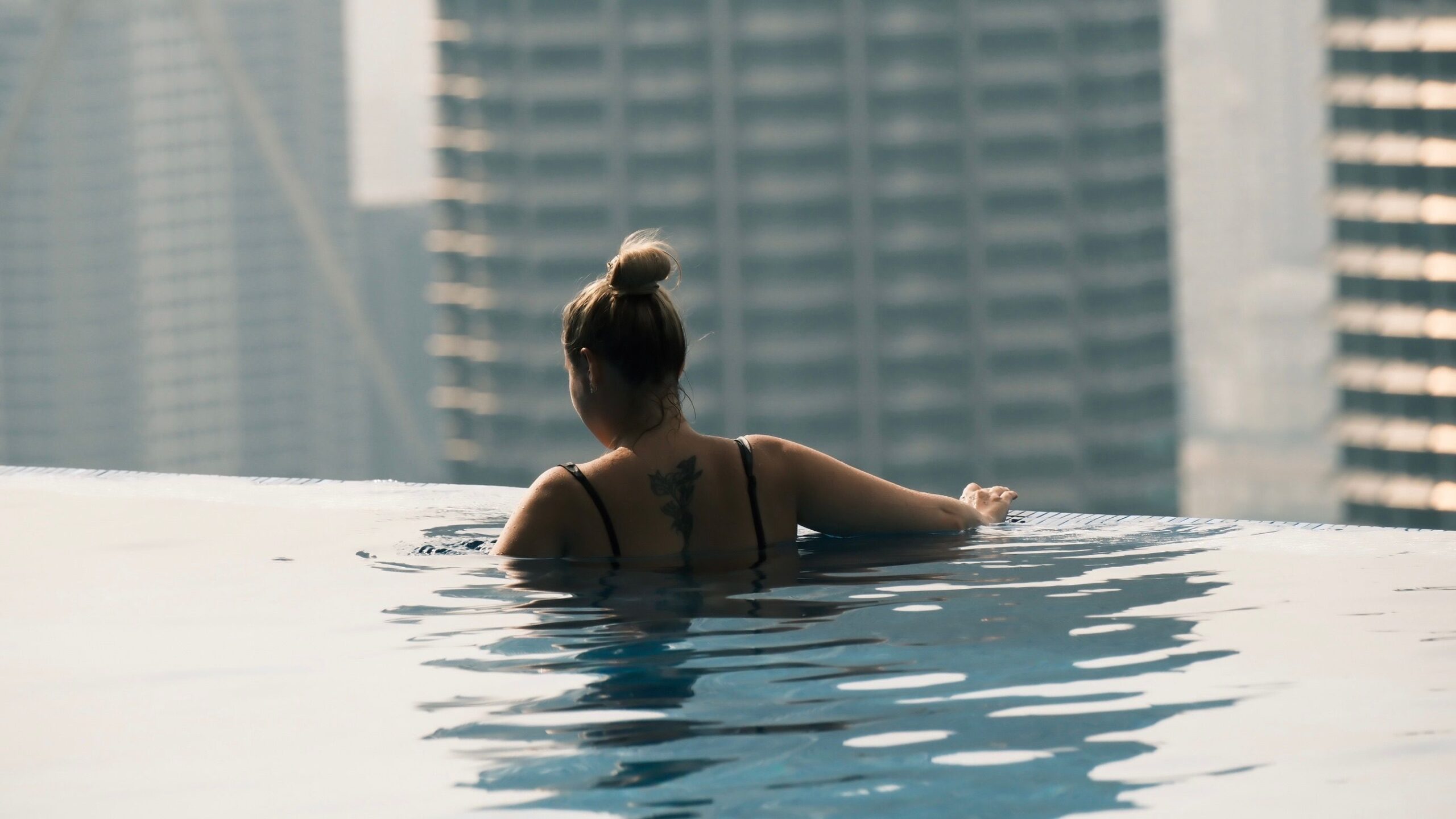 A woman enjoys a peaceful swim in a rooftop infinity pool overlooking a cityscape.