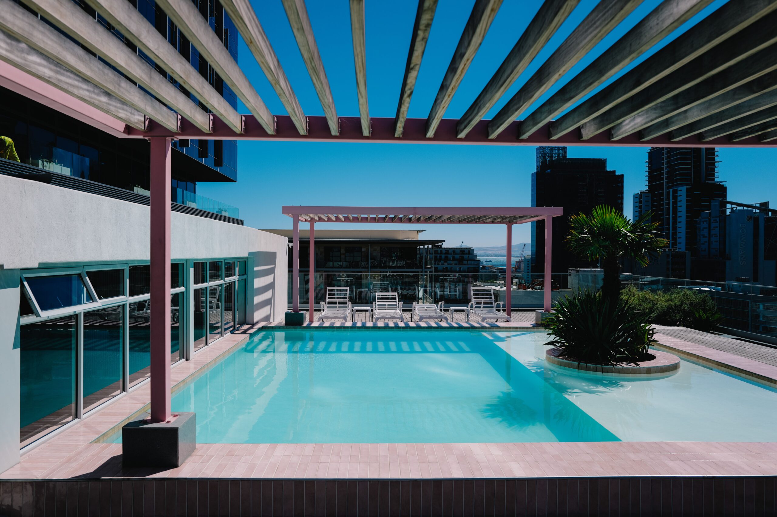 A stylish rooftop swimming pool with cityscape backdrop, featuring lounge chairs and pergolas.